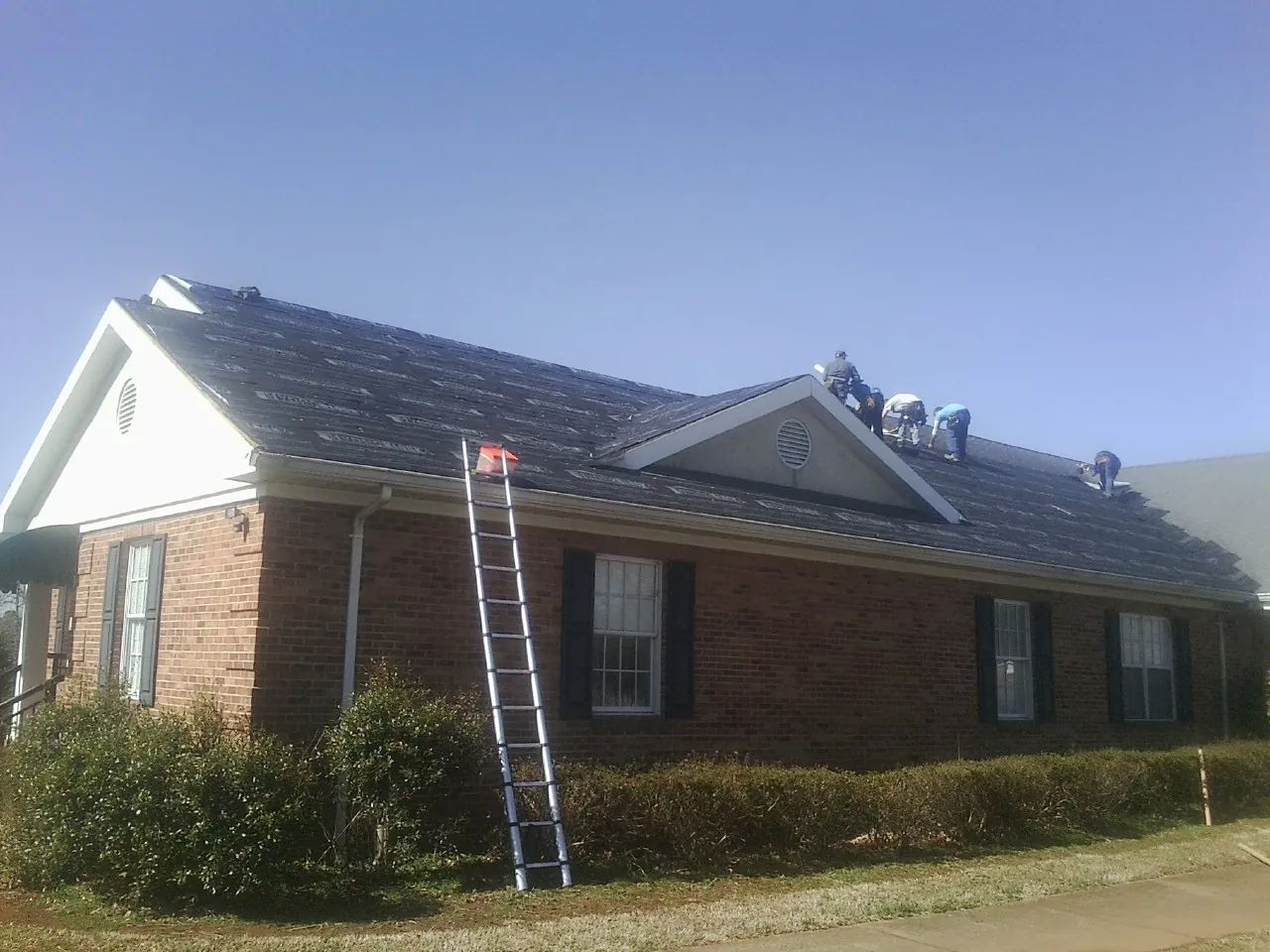 Crew tearing shingles off a brick ranch roof with a ladder set — Emergency Roof Repair work by our crew in Robesonia