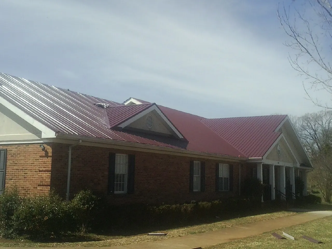 Red metal roof with gabled entries on a long brick building, from a Hail Damage Roof Repair job in Robesonia
