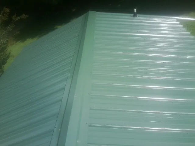 New green metal panels meeting at the ridge of a roof — Flat Roof Repair work by our crew in Robesonia