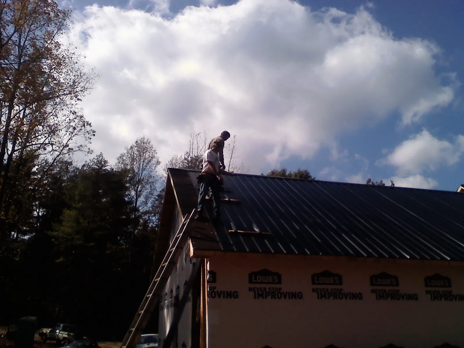 Roofer fastening dark metal panels high against a cloudy sky, from a Roof Inspection job in Robesonia