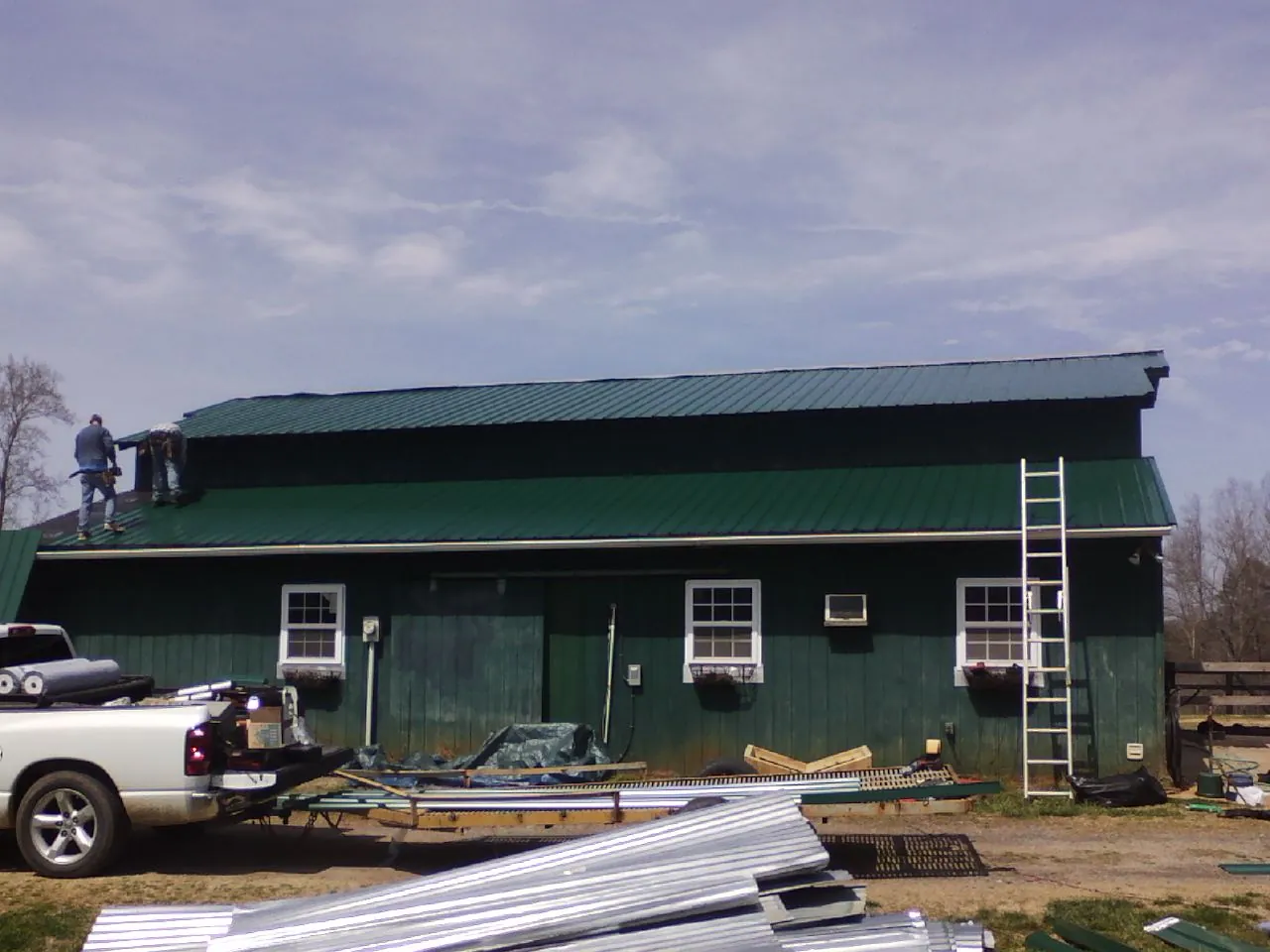 Crew installing green metal roofing on a large green barn in Robesonia