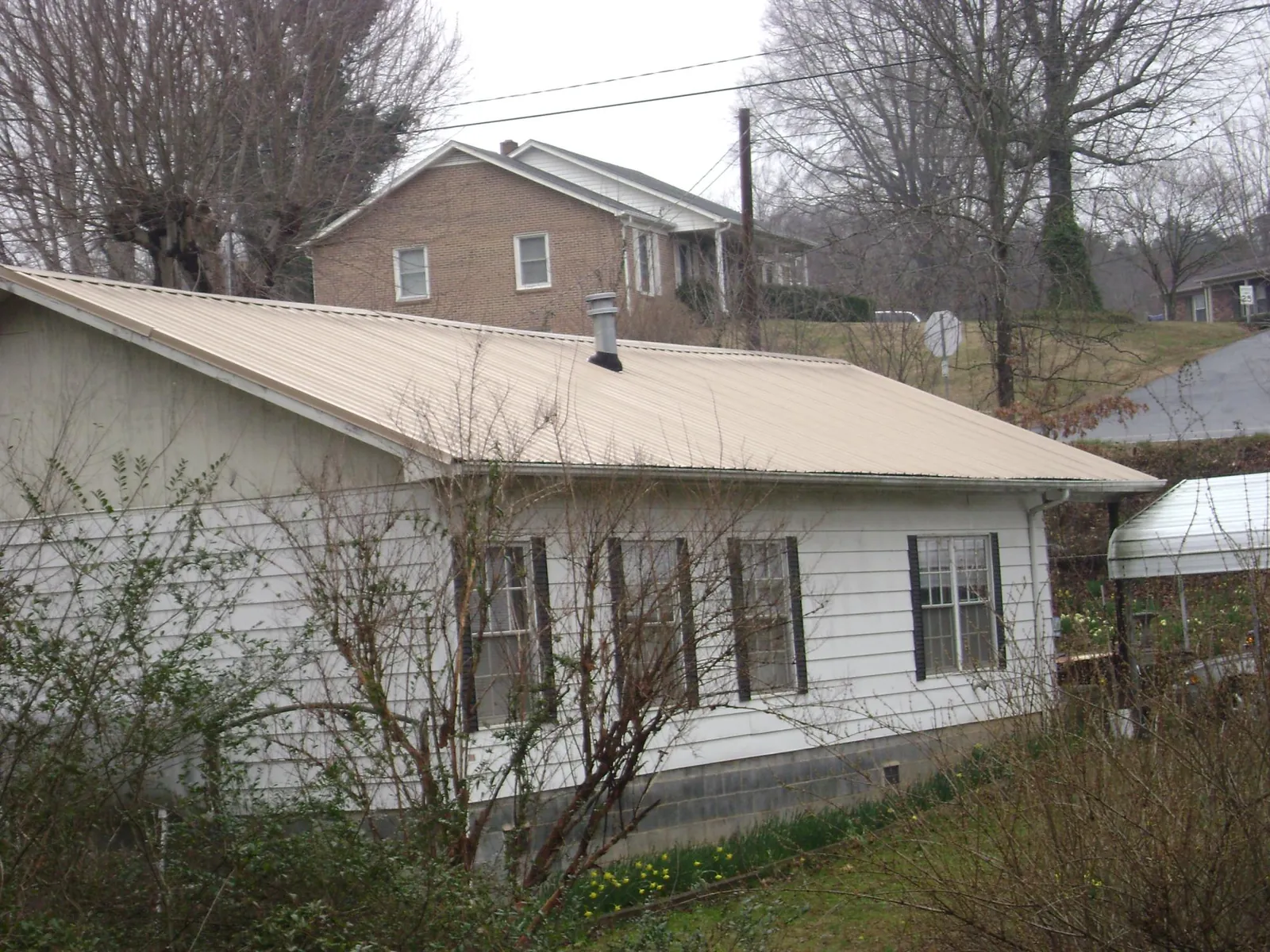 Tan metal roof on a white sided house set into a hillside — Commercial Roofing by Roofing Brothers in Robesonia
